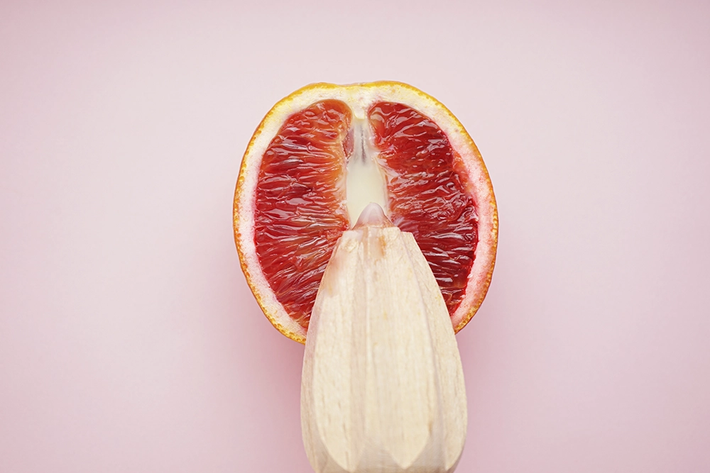 Moiti&eacute; d&rsquo;orange sanguine sur fond rose avec un presse-agrume pour symboliser un sextoy trop gros.