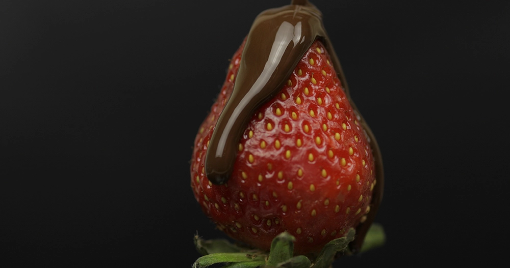 Coulis de chocolat sur une fraise pour illustrer les jeux et plaisirs sensoriels dans le couple.