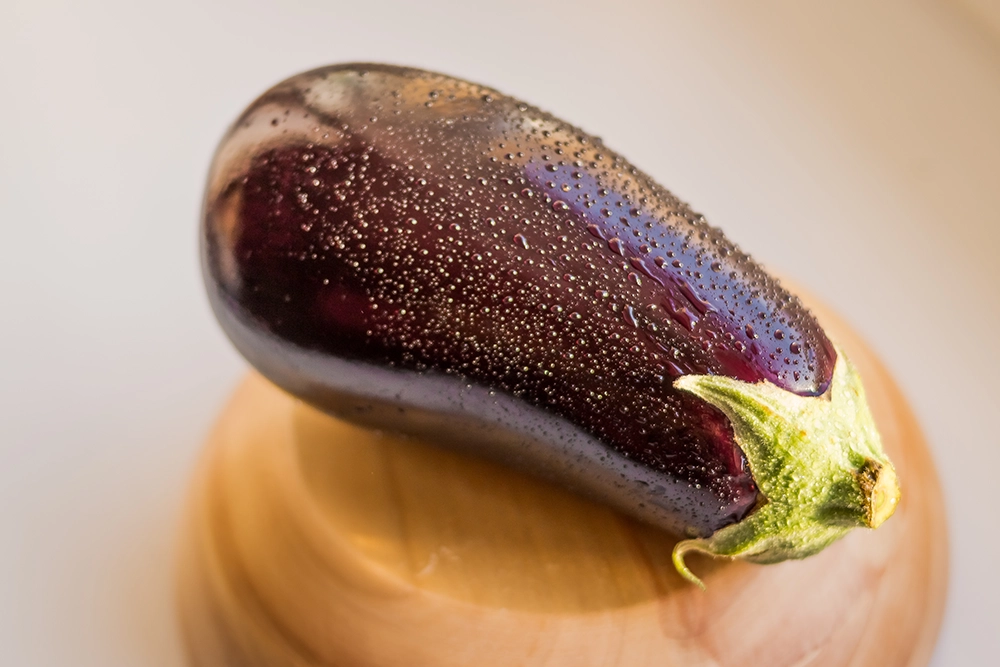 Gros plan d’une aubergine fraîche perlée de gouttelettes d’eau sur un fond clair.