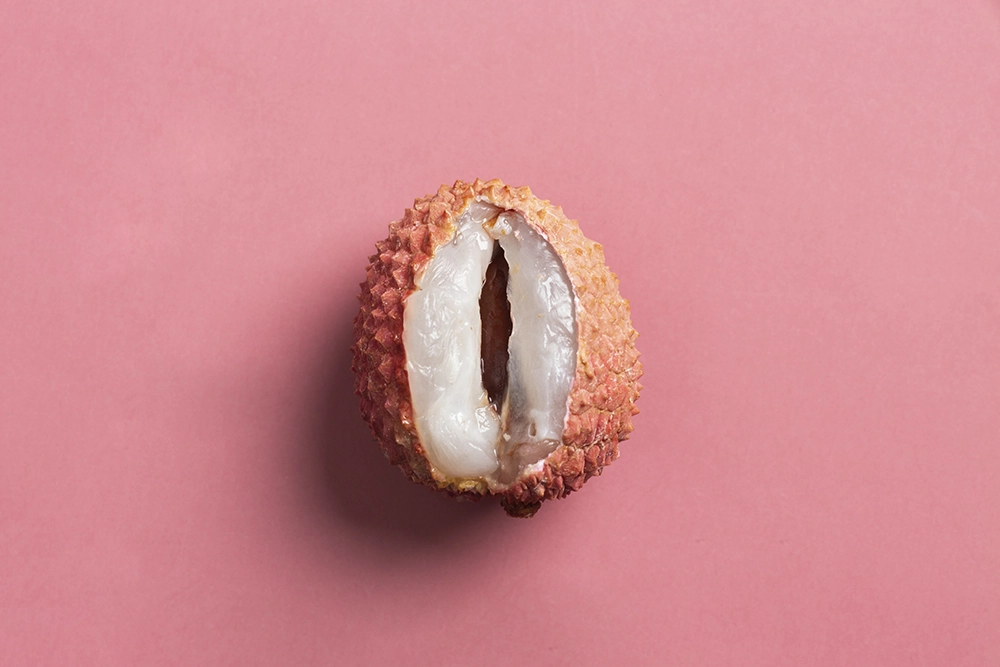  Litchi ouvert sur fond rose, symbolisant le titre &ldquo;Quel premier sextoy choisir, selon ses envies et besoins ?&rdquo;.