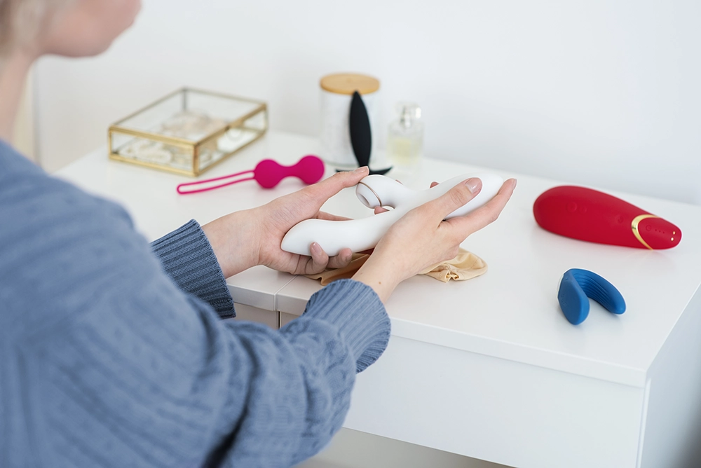 Jeune femme comparant diff&eacute;rents mod&egrave;les de sextoys pos&eacute;s sur une table de chevet. 